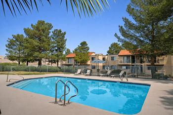 A swimming pool surrounded by trees and chairs.
